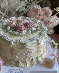 there is a white cake with pink flowers on the table next to lace doily