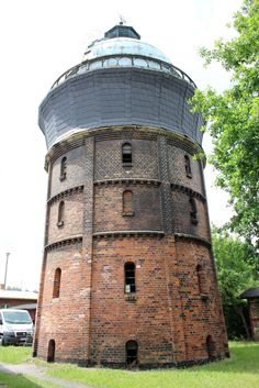 an old brick tower with a glass top in the middle of a grassy area next to trees