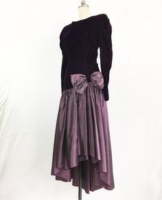 The perfect winter party dress! Long sleeve velvet deep purple bodice with a layered purple taffeta full skirt, adorned with a bow. The drop waist gives this dress a flapper feel. Asymetrical hemline, unlined, hidden zipper in the back. Deep V-back neckline. Gorgeous and ready for a fun night. DETAILS: Label: None Fabric: Velvet, Taffeta Lining: None Decade: 1980's MEASUREMENTS: Shoulders: 15'' Bust: 32'' Waist: 26'' Length: 48''front, 54''back Hips: 32'' Sleeves: 26'' Sleeve opening: 6'' widest Purple Velvet Dress For Party, Purple Velvet Party Dress, Elegant Purple Velvet Dress, Formal Purple Velvet Dress, High Low Cocktail Dress, Columbia Tn, Country Dresses, Party Dress Long Sleeve, Winter Party Dress