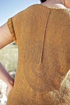 a woman wearing a brown sweater standing in a field with her back to the camera