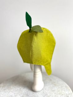 an apple shaped hat on top of a white mannequin headdress with green leaves