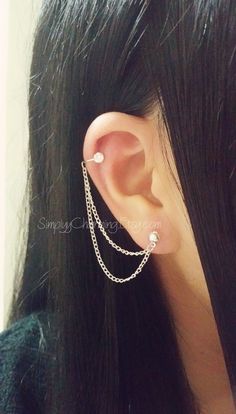 a woman with long black hair wearing a pair of ear piercings and chain earrings