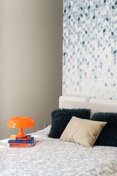 a bed with two pillows and an orange lamp on it's headboard in front of a patterned wall