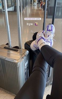 a woman is sitting on her luggage at the airport with her feet propped up next to her suitcase