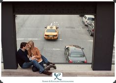 a man and woman are sitting on the edge of a window looking at cars in traffic