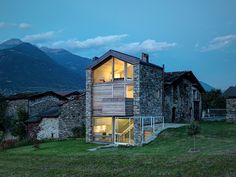 the house is made out of stone and has glass windows on each floor, while it's surrounded by green grass