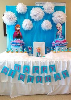 a table topped with cake and decorations for a frozen princess birthday party that includes pom poms