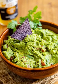 a wooden bowl filled with guacamole and a purple tortilla chip