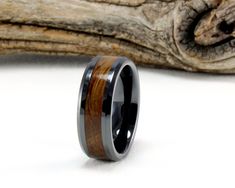 a black ceramic ring with wood inlays on it and a piece of driftwood behind it