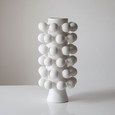 a white vase sitting on top of a table next to a wall with balls all over it