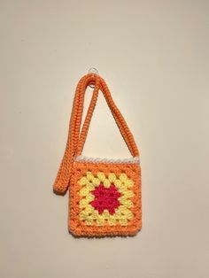 an orange and yellow crocheted purse hanging on a wall with a white background