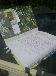 an open notebook sitting on top of a table next to a swimming pool with papers and pens