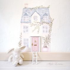 a white stuffed animal sitting in front of a doll house with pink door and window