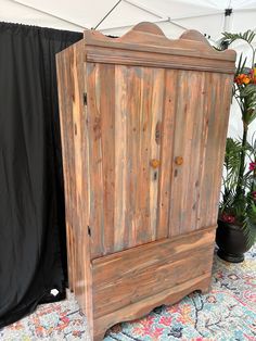 a wooden cabinet sitting on top of a rug next to a potted plant in front of a black curtain