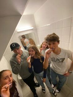 a group of young people brushing their teeth in a bathroom with white tiles on the walls