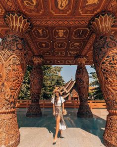 a woman standing under an ornate wooden structure