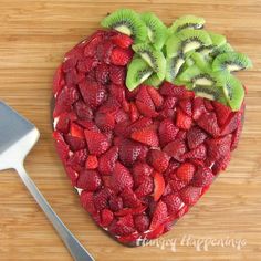 a heart shaped cake with sliced kiwis and strawberries on the side next to a knife