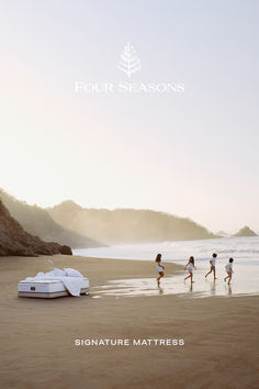 four people running on the beach near an inflatable mattress