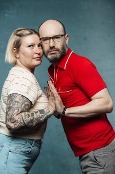 a man and woman standing next to each other in front of a blue background with tattoos on their arms