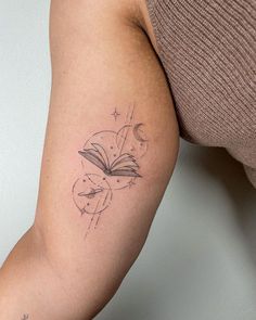 a woman's arm with a book and stars tattoo on the left side of her arm