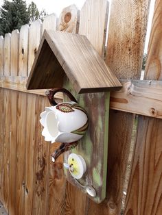 a wooden fence with a bird house on it and two cups hanging from the side