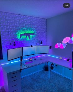 a computer desk with two monitors on top of it in front of a neon wall