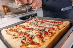 a person is sprinkling cheese on top of a pizza in a pan at a kitchen counter