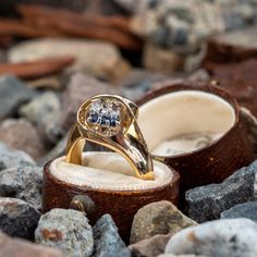 an engagement ring sitting on top of a wooden box surrounded by rocks and stones,