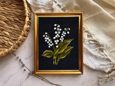 a painting of lily of the valley in a gold frame on a white marble surface