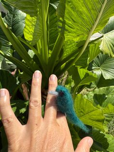 a person's hand with a needle in the middle of some leaves and a plant