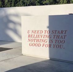 a white wall with a red quote on it next to a parking meter and trees