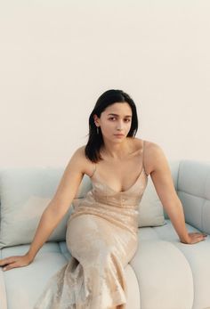 a woman sitting on top of a white couch wearing a gold dress and posing for the camera