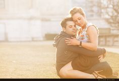 a man and woman sitting on the ground in front of a building hugging each other