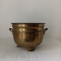 an antique brass bowl with handles on a white tableclothed surface, ready to be used as a centerpiece