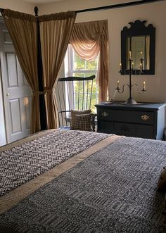 a bedroom with a bed, dresser and mirror in front of a window that has curtains on it