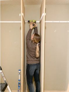 a woman is using a drill to install the wall in her closet with no doors