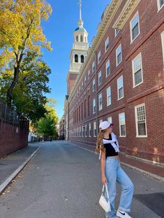 a woman is walking down the street in front of an old brick building with a steeple on top