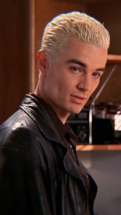 a young man with blonde hair wearing a black leather jacket and looking at the camera