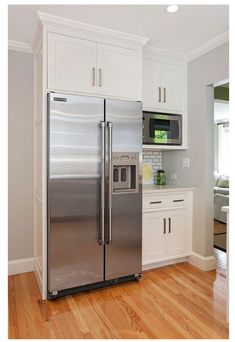 a silver refrigerator freezer sitting inside of a kitchen next to white cabinets and wooden floors