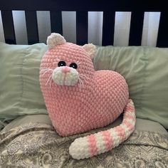 a crocheted pink cat laying on top of a bed next to green pillows