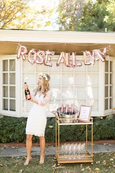 a woman standing in front of a table holding a bottle of wine with rose all down on it