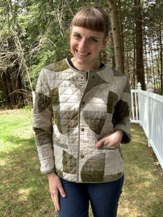 a woman standing in front of a fence wearing a quilted jacket and smiling at the camera