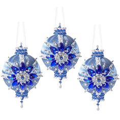 three blue christmas ornaments hanging from strings on a white background with snowflakes and crystals