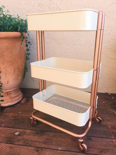 a three tiered metal rack with two baskets on it next to a potted plant