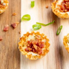 mini pizzas with bacon and green onions on a wooden table next to other small food items