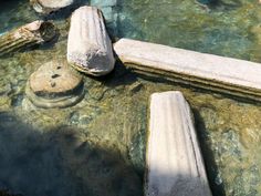 two stone benches sitting on top of a body of water next to rocks and boulders