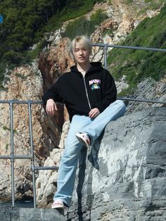 a young man sitting on top of a metal railing next to a rocky mountain side