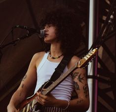 a man with curly hair playing guitar on stage at an outdoor concert or gathering area