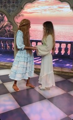 two women standing on a checkered floor in front of an ocean view at sunset