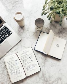 an open notebook sitting on top of a table next to a laptop computer and coffee cup